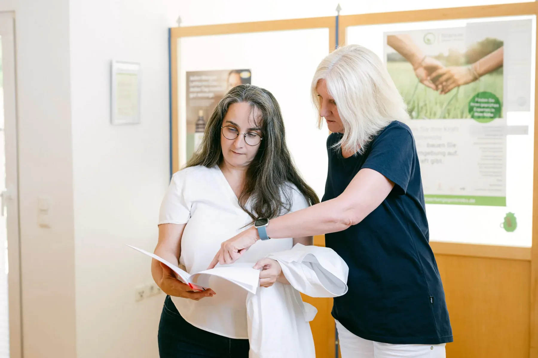 Zwei Frauen prüfen gemeinsam einen ausgedruckten Bericht. Die Dame auf der rechten Seite, scheint ihre Kollegin auf eine bestimmte Stelle hinzuweisen.