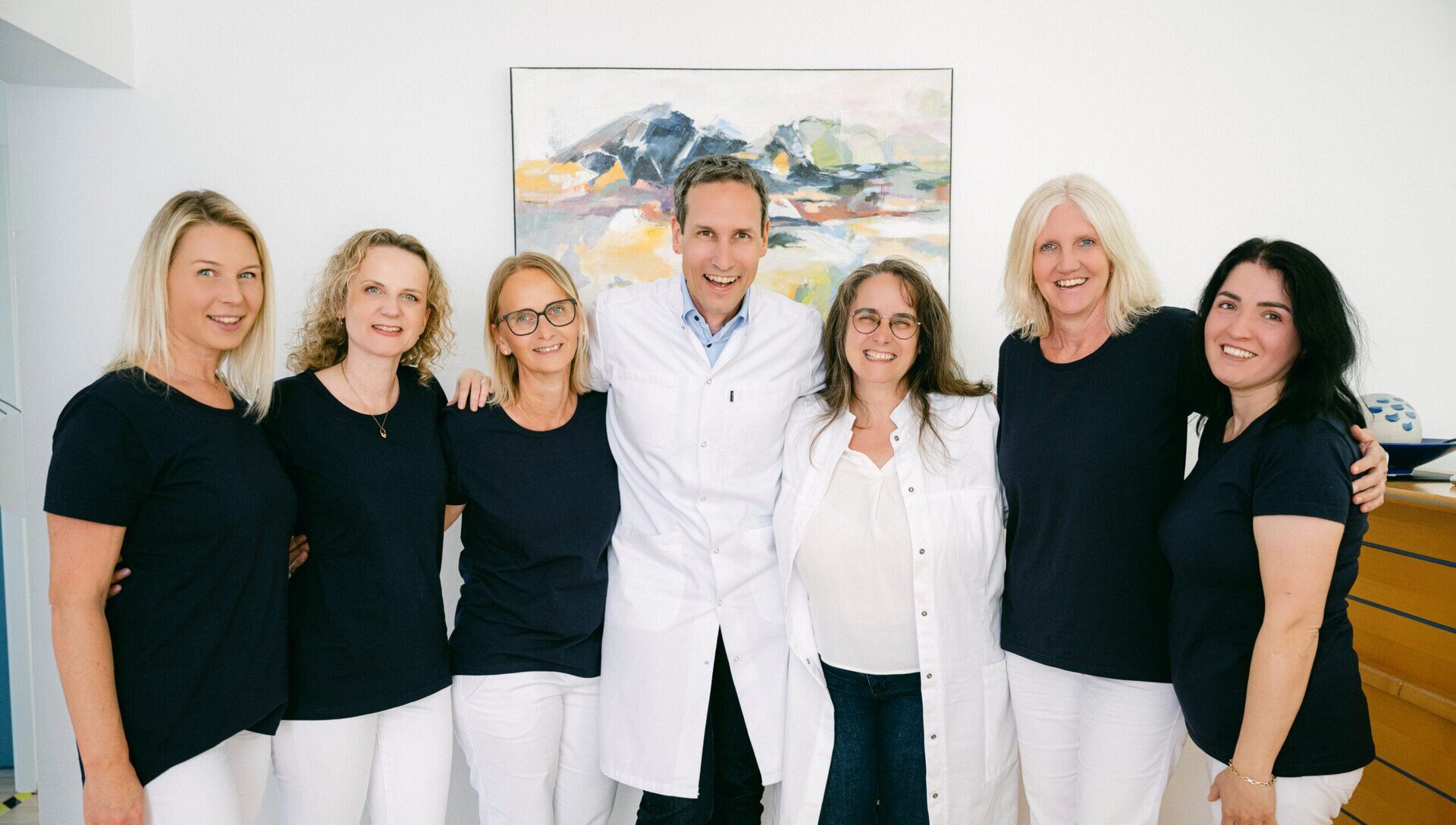 Das Team der Praxis ist zu sehen. Sie stehen Arm in Arm nebeneinander und lächeln in die Kamera.