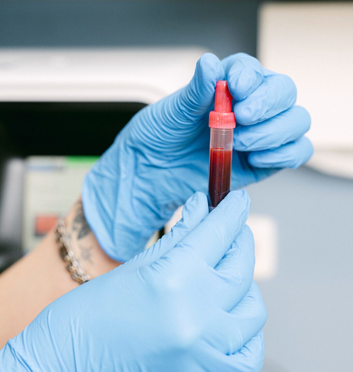 Eine Phiole voll Blut ist zu sehen, die von einer MFA mit Gummihandschuhen in der Hand gehalten wird.